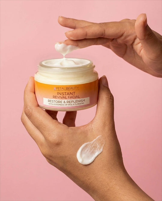 Hand applying cream from a 'Petals Beauty' jar against a pink background